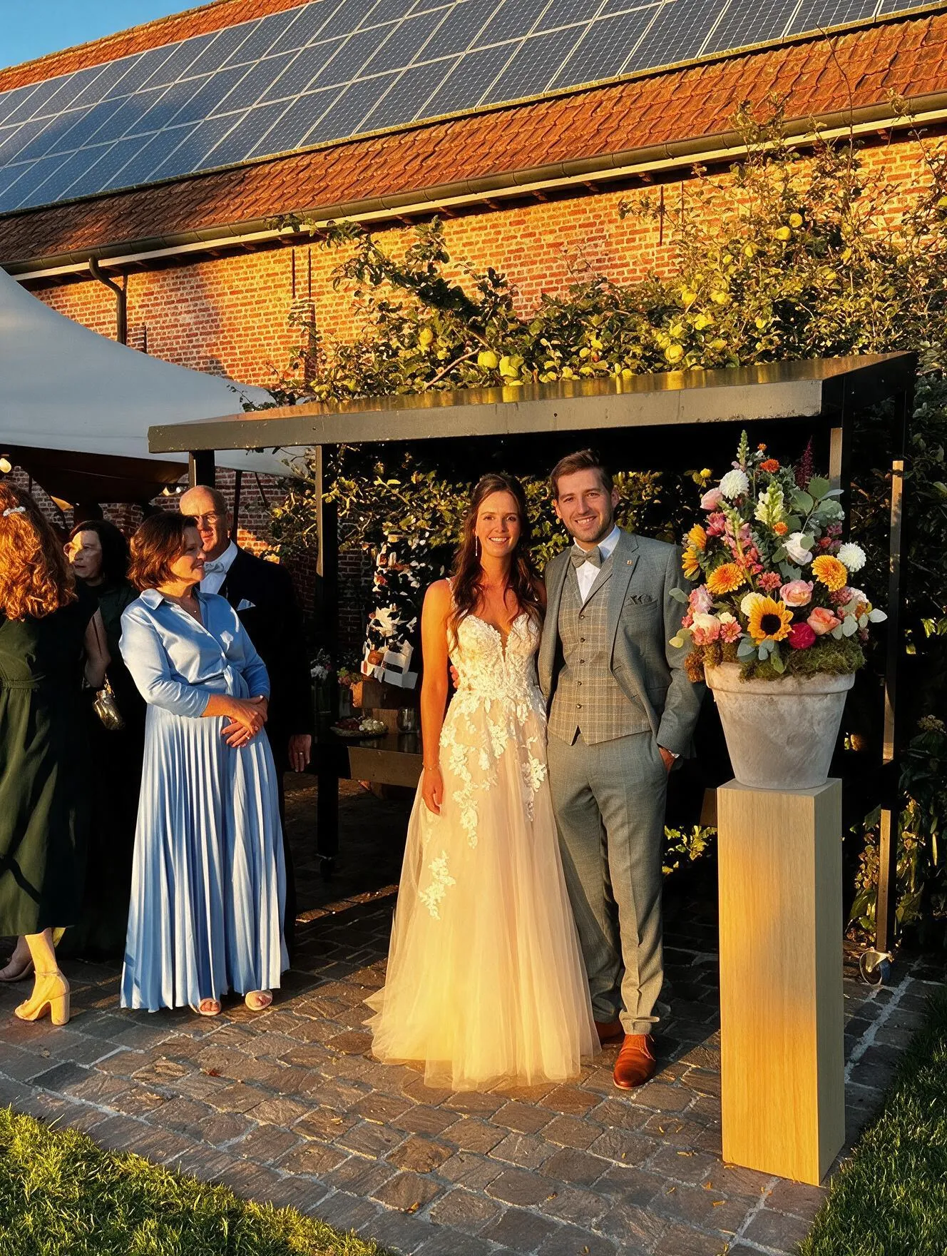 Bruidspaar in de avondzon bij een bloemstuk op de koer van Speghelhof