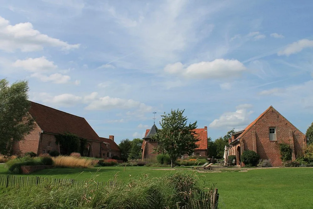 Overzicht van het domein Speghelhof met de historische hoevegebouwen rond de weide onder een weidse lucht