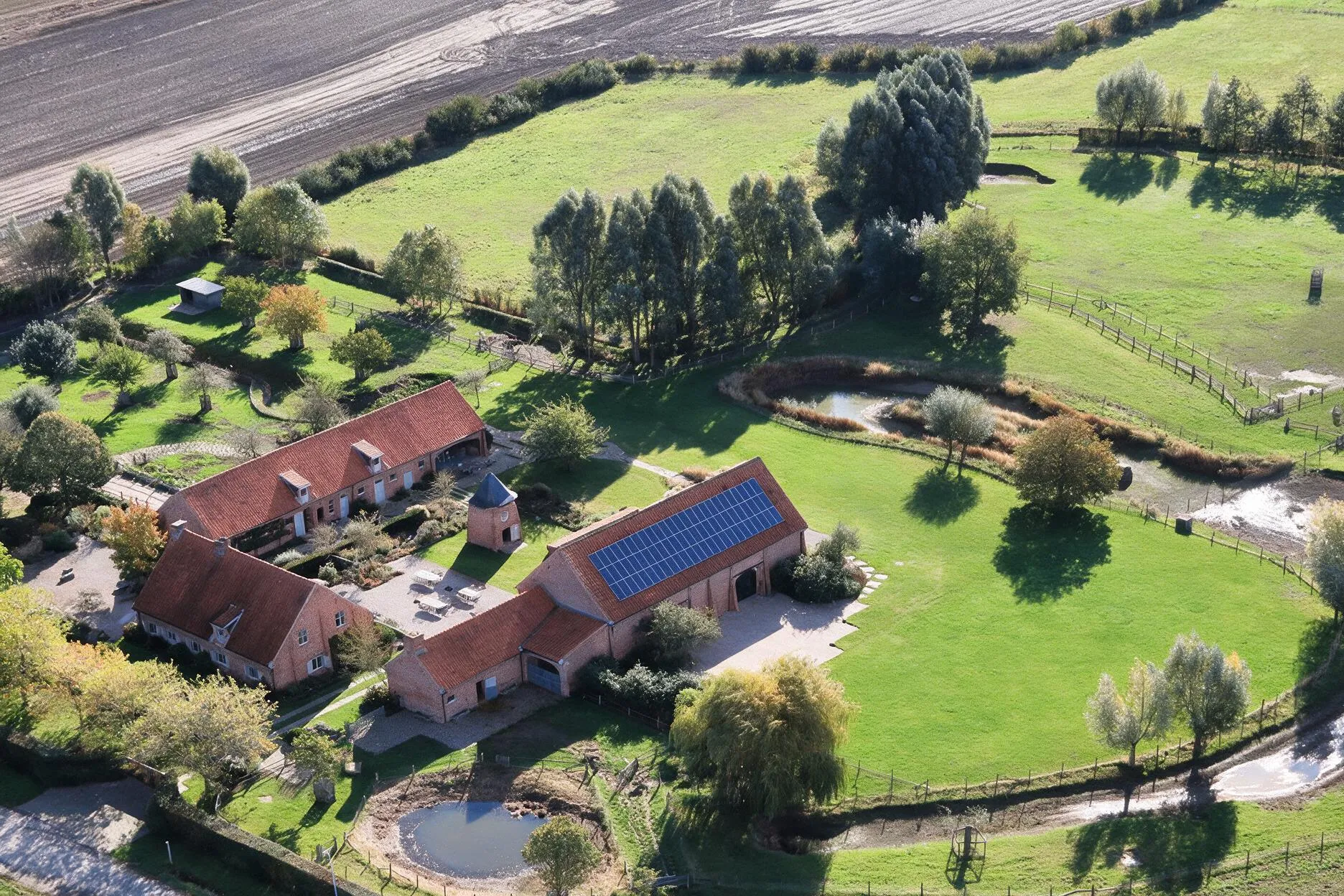Luchtfoto van het domein Speghelhof met hoeve, feestschuur, vijvers en weides tussen de velden in Wervik