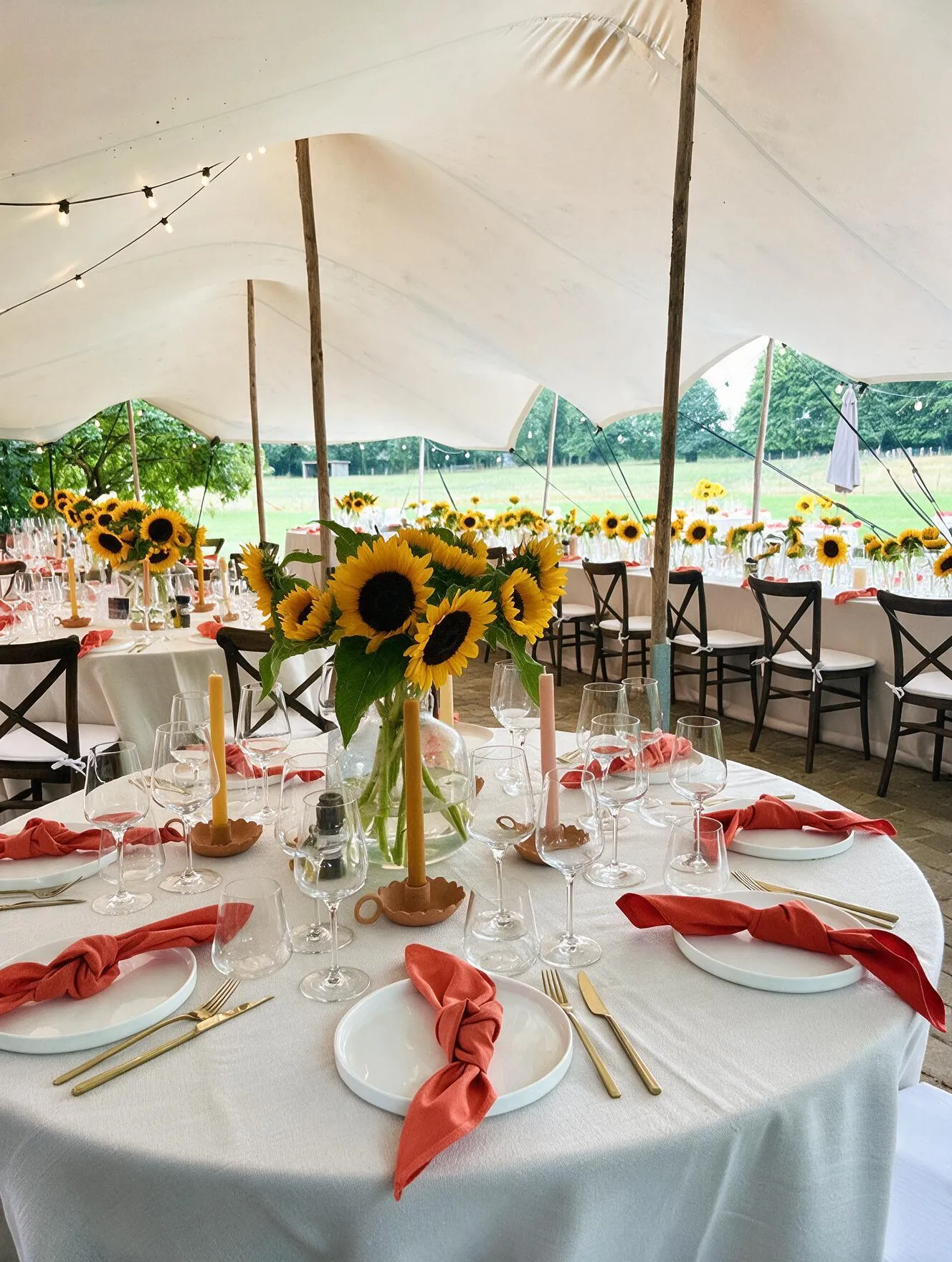 Gedekte tafel met zonnebloemen en koraalrode servetten onder de tent op Speghelhof